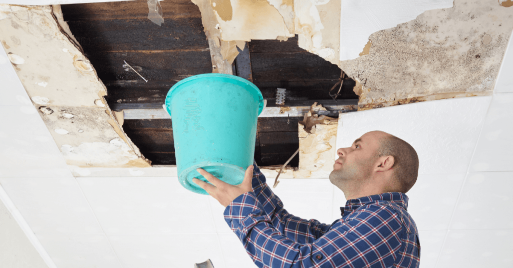 A man containing a roof leak with a bucket.
